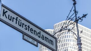 Stadtrundgang Kurfürstendamm – Straßenschild Ku'damm mit Upper West Hochhaus in der City West Berlin