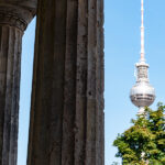 Berlin TV Tower next to the colonnades of Museum Island under a blue sky.